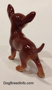 The back left side of a brown with white Chihuahua figurine. The figurine is glossy.